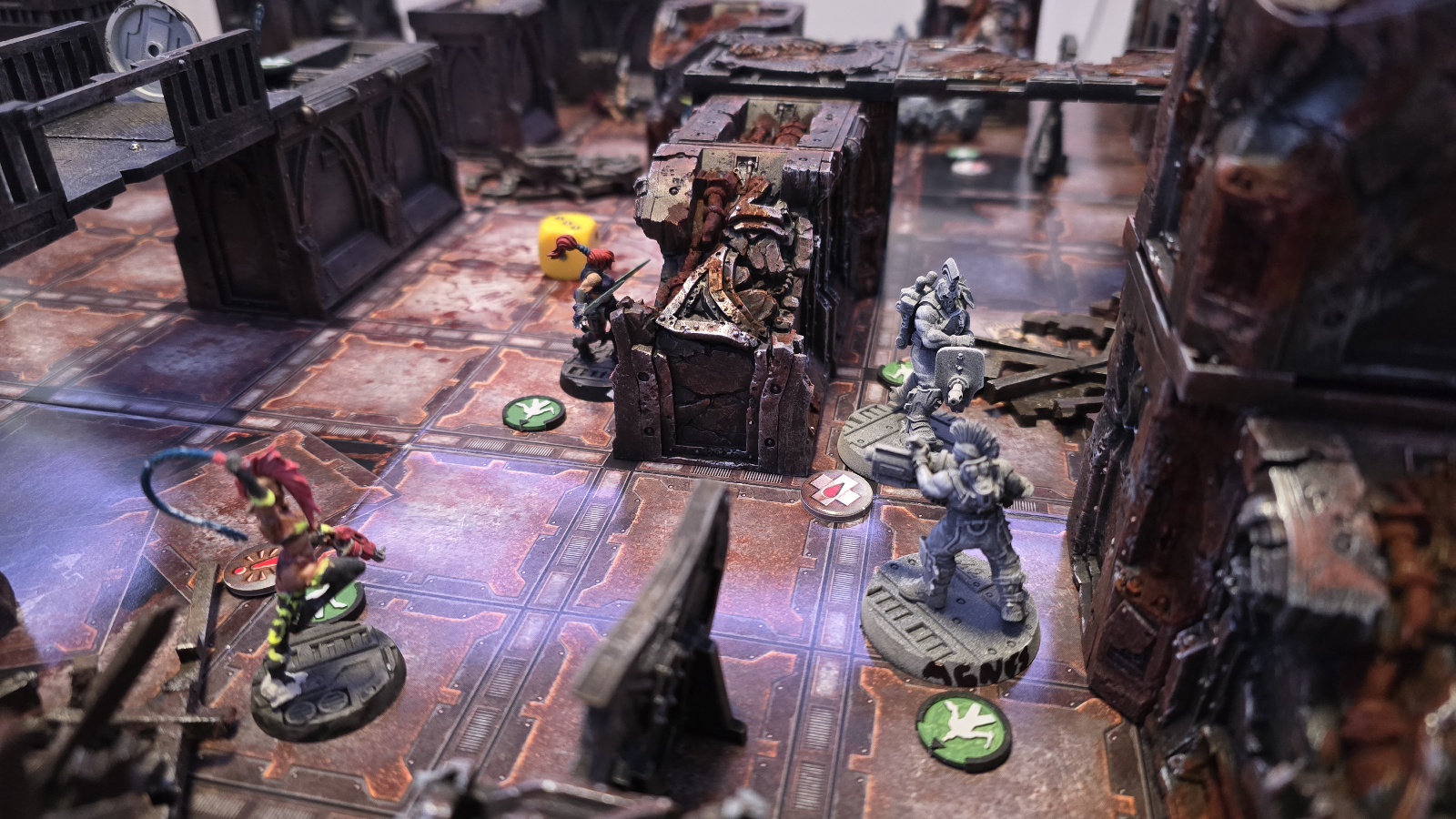 Spelbräde för Necromunda med flera målade miniatyrfigurer i en industriell stadsruinmiljö, med gångbroar, barriärer och markörer på ett rutigt underlag.
